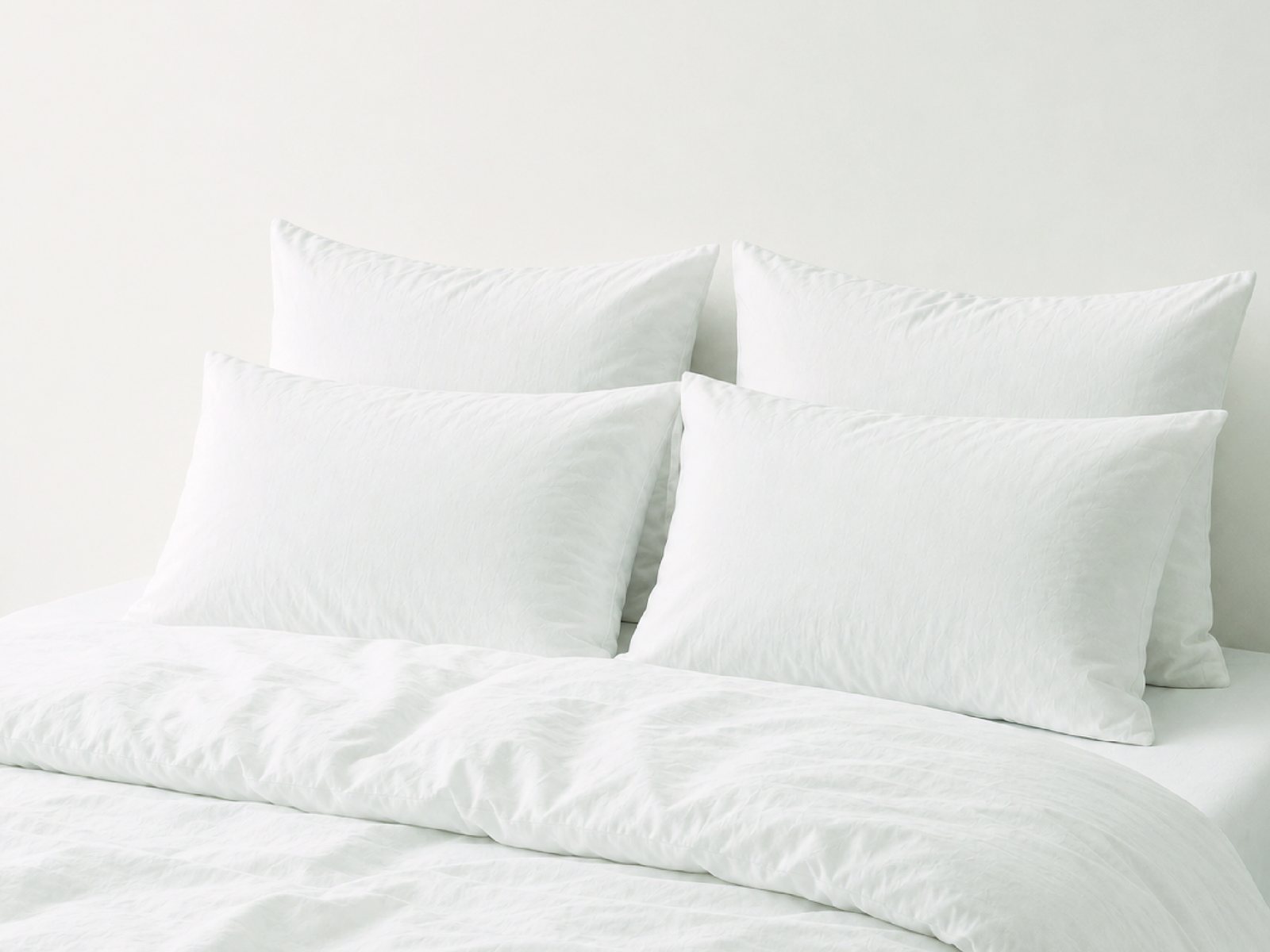 A made bed in white cotton — four pillows against the headboard, the duvet turned back