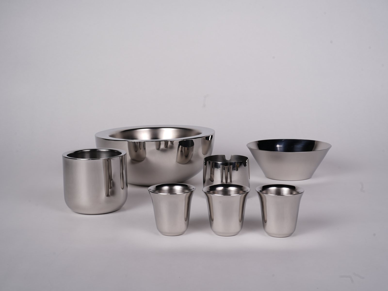 The Meteorite family in stainless steel — a large bowl, a blackened bowl and six tumblers on a pale ground